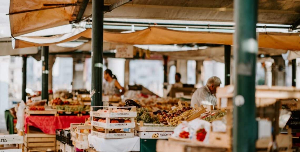 foodmarket | crowdfundingde Bunte Stände auf einem Markt mit frischem Obst und Gemüse umgeben von Verkäufern und Besuchern